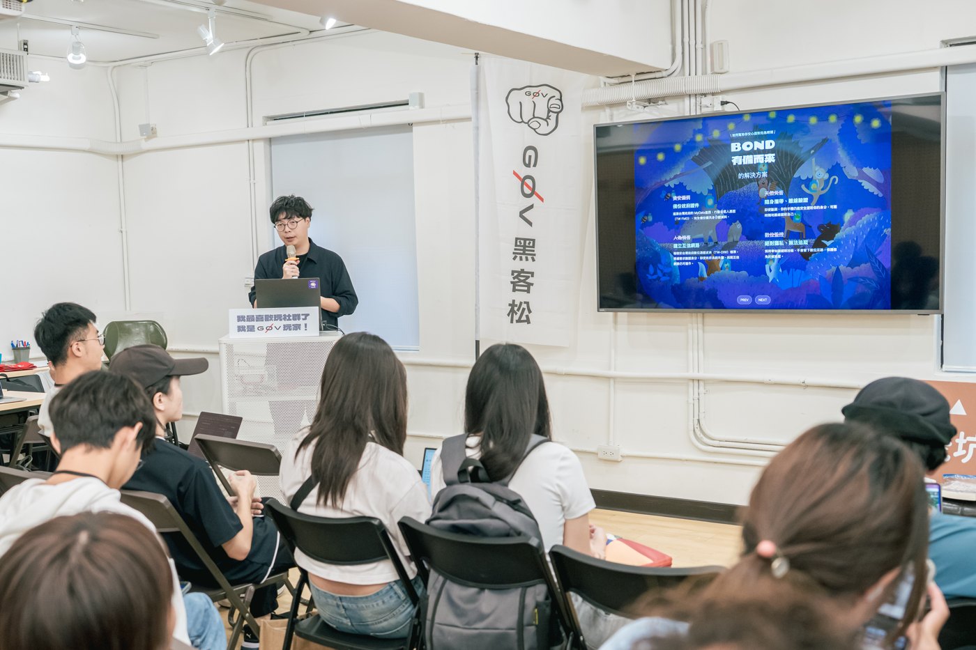 Participants at the g0v hackathon watch the Bond team’s public presentation, with BOND visible on the front projection.